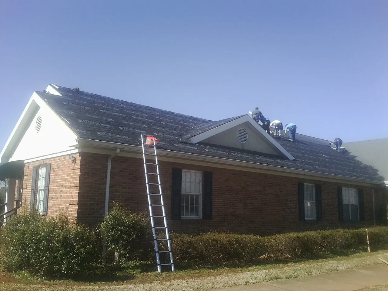 Crew tearing shingles off a brick ranch roof with a ladder set — Metal Roof Repair work by our crew in Williamstown