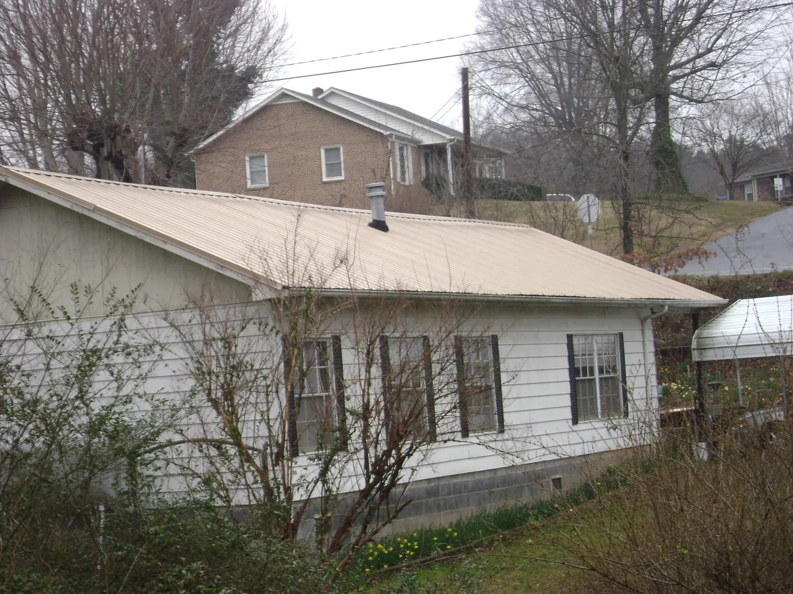 Tan metal roof on a white sided house set into a hillside — Commercial Roofing by Roofing Brothers in Williamstown